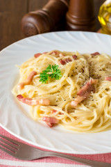 Classic pasta carbonara. Spaghetti with bacon, egg yolk and parmesan cheese on white plate on dark wooden background.