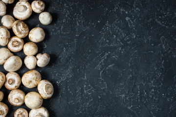 Fresh champignon mushrooms on dark background, top view with copy space