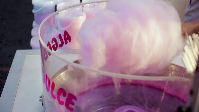 Delicious calrie rich pink cotton candy machine in use, with sugar being broken into pieces to create airy tasty sweet treat for kids or adults on county fair or at amusement park during summer break