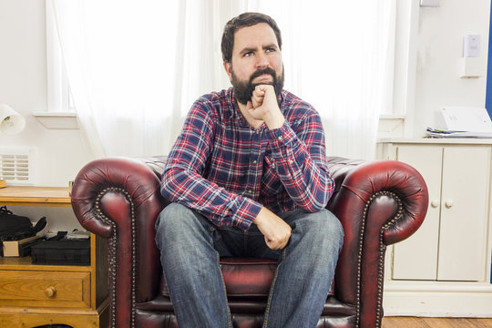 Thoughtful White Man Sitting In Red Arm Chair