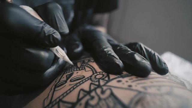 Macro view on professional tattoo master is painting tattoo with black ink, making cover. Works in black latex gloves with handmade rotor gun machine in his studio