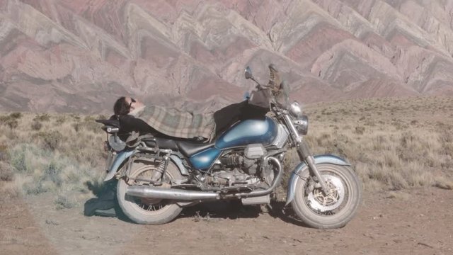 Woman resting on blue motorcycle on a bright day on the mountains of  Argentina.