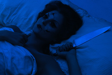Spooky porcelain speaking doll holding knife and lying in the bed