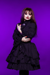 Witch, a vampire in a black gothic dress on a purple background. American, dress for a costume party Halloween. Bright makeup