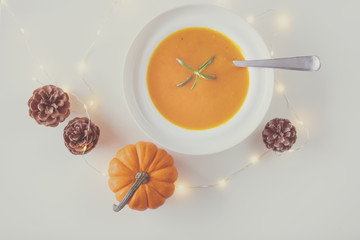 Pumpkin soup with rosemary in white plate near a pine cone with Fairy Ligths