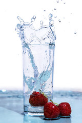 Strawberries fall into a glass of water.