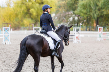 Young rider woman on bay horse warming up before advanced dressage test at equestrian competition....