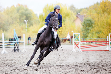 Young rider man on bay horse galloping on his course at show jumping competition