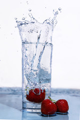 Strawberries fall into a glass of water.