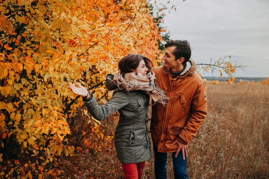 Young Couple Walks In Autumn Forest Among Colorful Trees