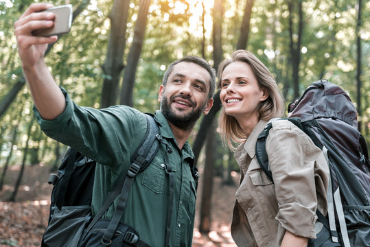 Happy man and woman photographing themselves on smartphone in nature