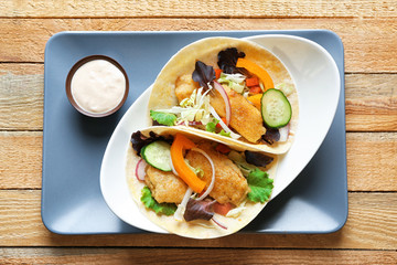 Plate with delicious fish tacos and sauce on wooden background