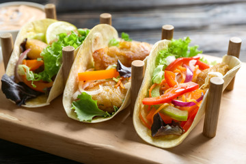 Wooden holder with delicious fish tacos on table, closeup