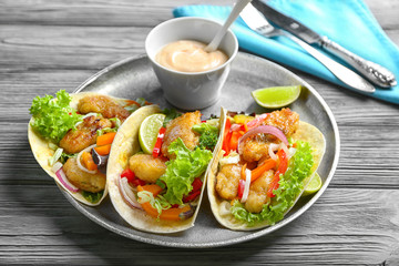 Plate with delicious fish tacos on wooden table