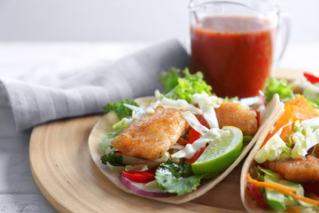Wooden plate with delicious fish tacos on table, closeup