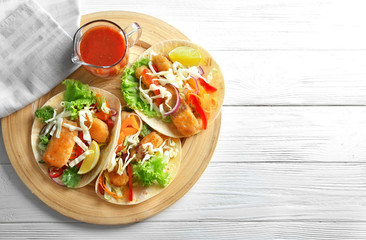 Wooden plate with delicious fish tacos on table
