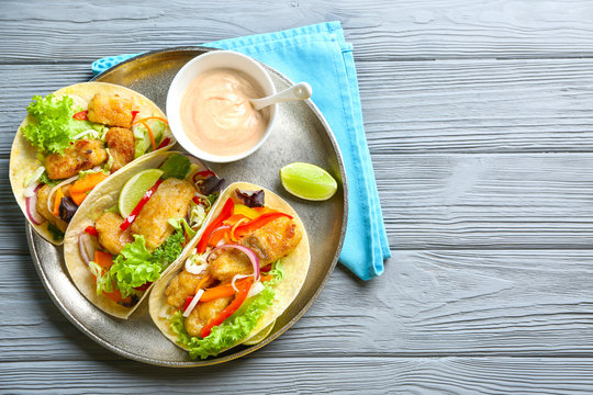 Plate with delicious fish tacos on wooden table