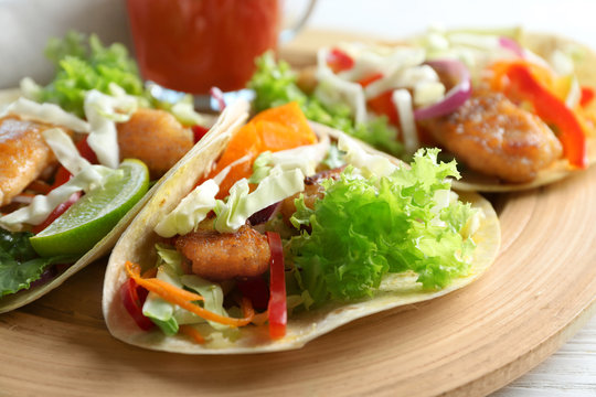 Wooden plate with delicious fish tacos on table, closeup