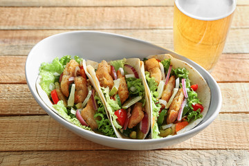 Bowl with delicious fish tacos on wooden table