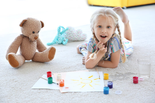 Cute little girl painting picture and spilled water on carpet