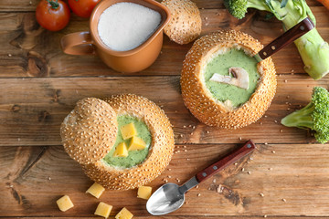 Broccoli cheese soup in bread buns on wooden table