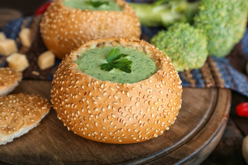 Broccoli cheese soup in bread bun on wooden board