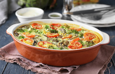 Baking dish with tasty broccoli casserole on wooden table