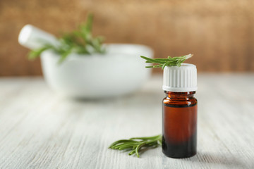 Bottle with rosemary oil and herb on wooden table