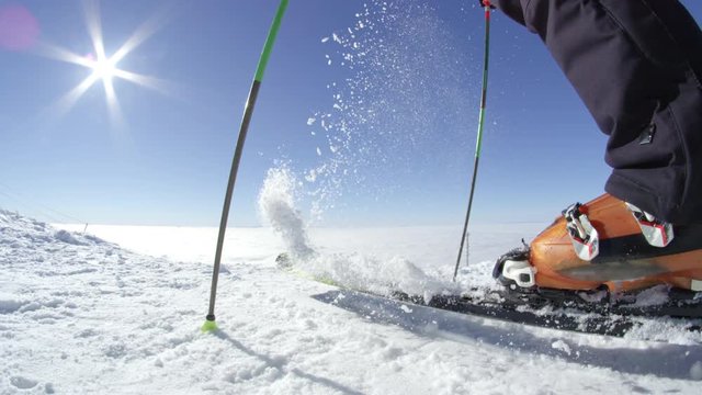 SLOW MOTION FISHEYE: Recreational skier removes freshly fallen snow from his skis on a top of the mountain above fog. Located at European ski resort in the Alps on a sunny cloudless winter day