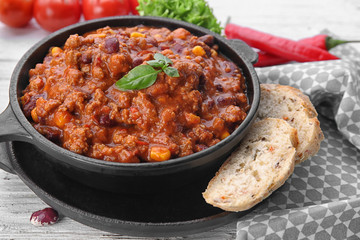 Chili con carne with fresh basil in frying pan on kitchen table