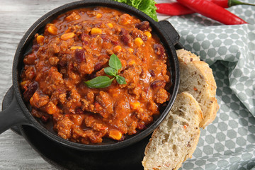 Chili con carne with fresh basil in frying pan on kitchen table