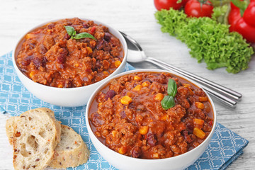 Chili con carne with fresh basil in bowls on kitchen table