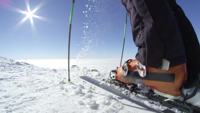 SLOW MOTION CLOSE UP: Skier removing fresh snow from skis on a top of the mountain above fog at European ski resort in the Alps on a sunny perfect cold and cloudless winter day with no people