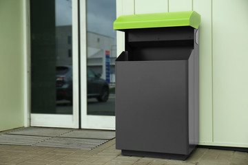 Modern garbage bin near entrance to building, outdoors