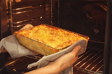 Woman taking baking tray with spinach lasagna out of oven