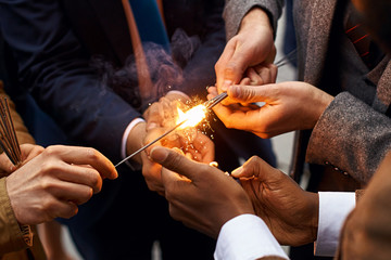 Hands of young people in suits holding burning sparkles fireworks