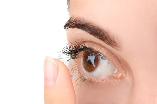 Young woman putting contact lens on light background, closeup