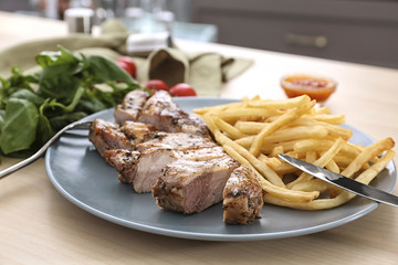 Plate with delicious grilled steak frites wooden table
