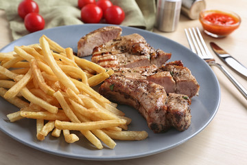 Plate with delicious grilled steak frites wooden table