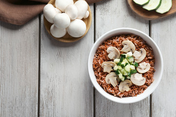 Bowl with tasty brown rice, zucchini and mushrooms on wooden table