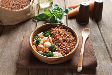 Bowl with tasty brown rice and vegetables on wooden table