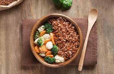 Bowl with tasty brown rice and vegetables on wooden table