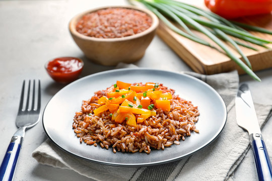 Plate with tasty brown rice and vegetables on table