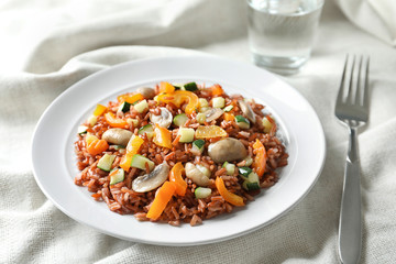 Plate with tasty brown rice, mushrooms and vegetables on table