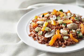 Plate with tasty brown rice, mushrooms and vegetables on table, closeup