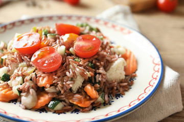 Plate with tasty brown rice and vegetables on table, closeup