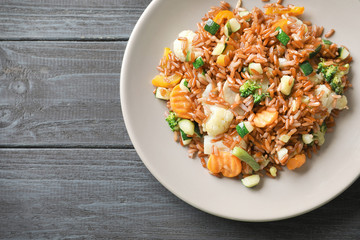 Plate with tasty brown rice and vegetables on wooden table