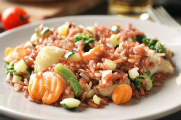 Plate with tasty brown rice and vegetables on table, closeup
