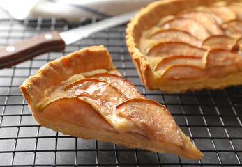 Cooling rack with piece of tasty pear tart on table