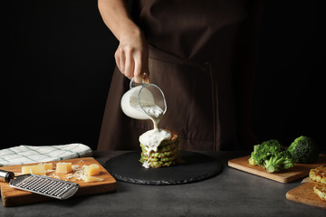 Woman pouring sauce onto tasty broccoli pancakes at table